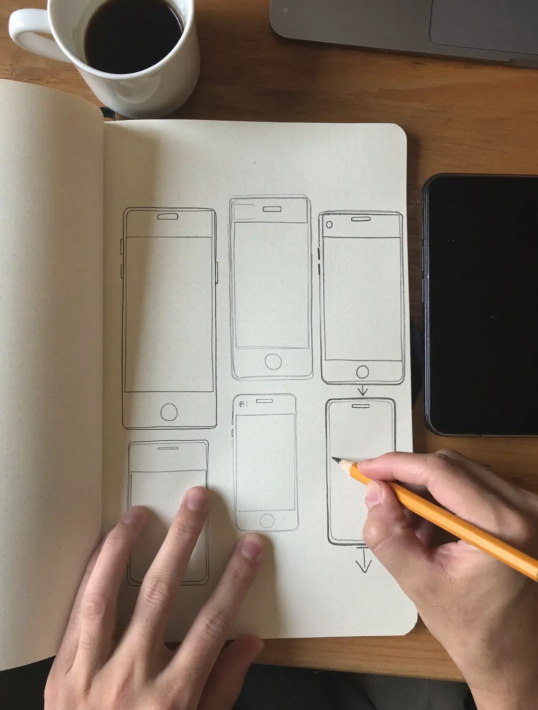 Hände skizzieren App-Bildschirme mit Bleistift in einem Notizbuch